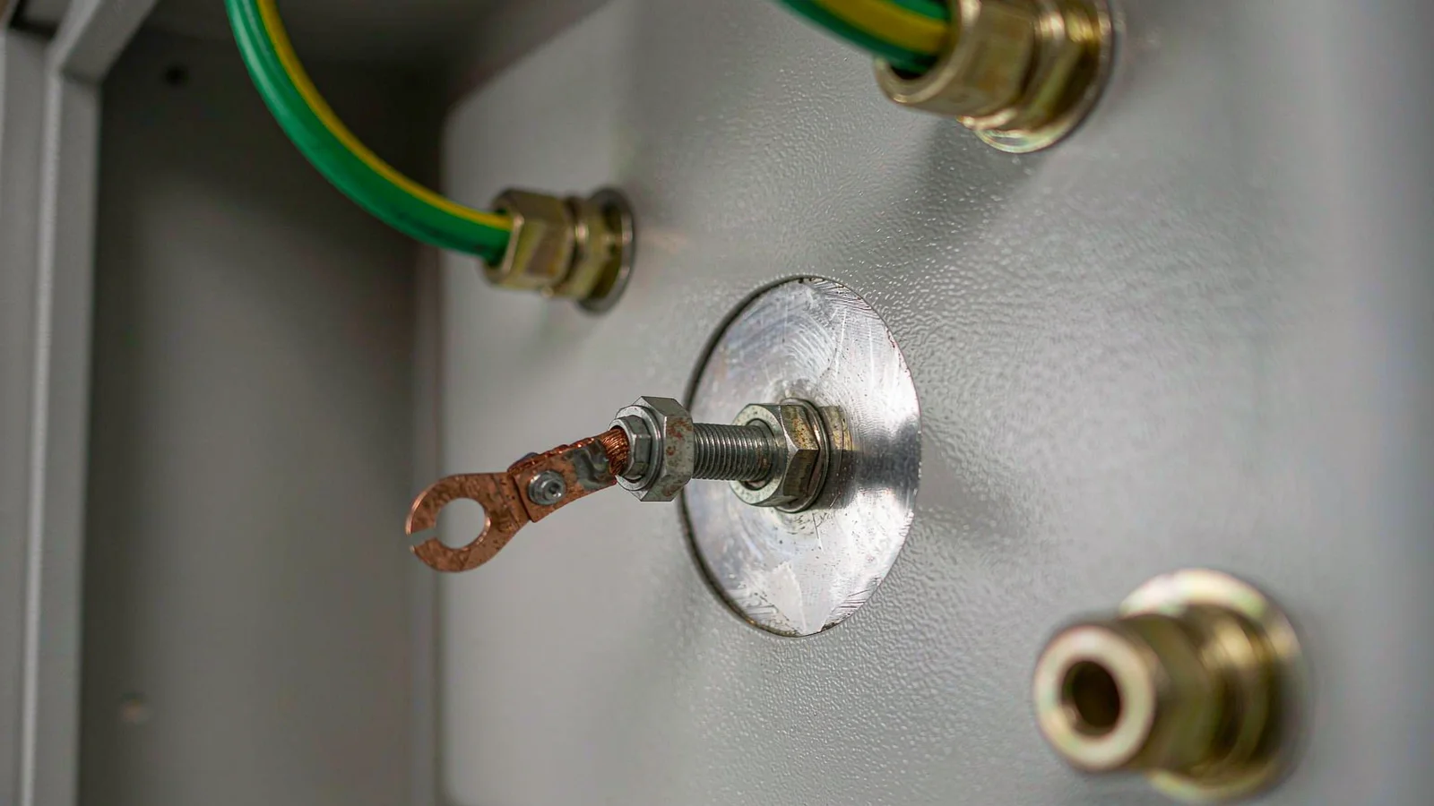 Bare masked steel pad around an earth stud in a painted cabinet wall with a brass gland nearby