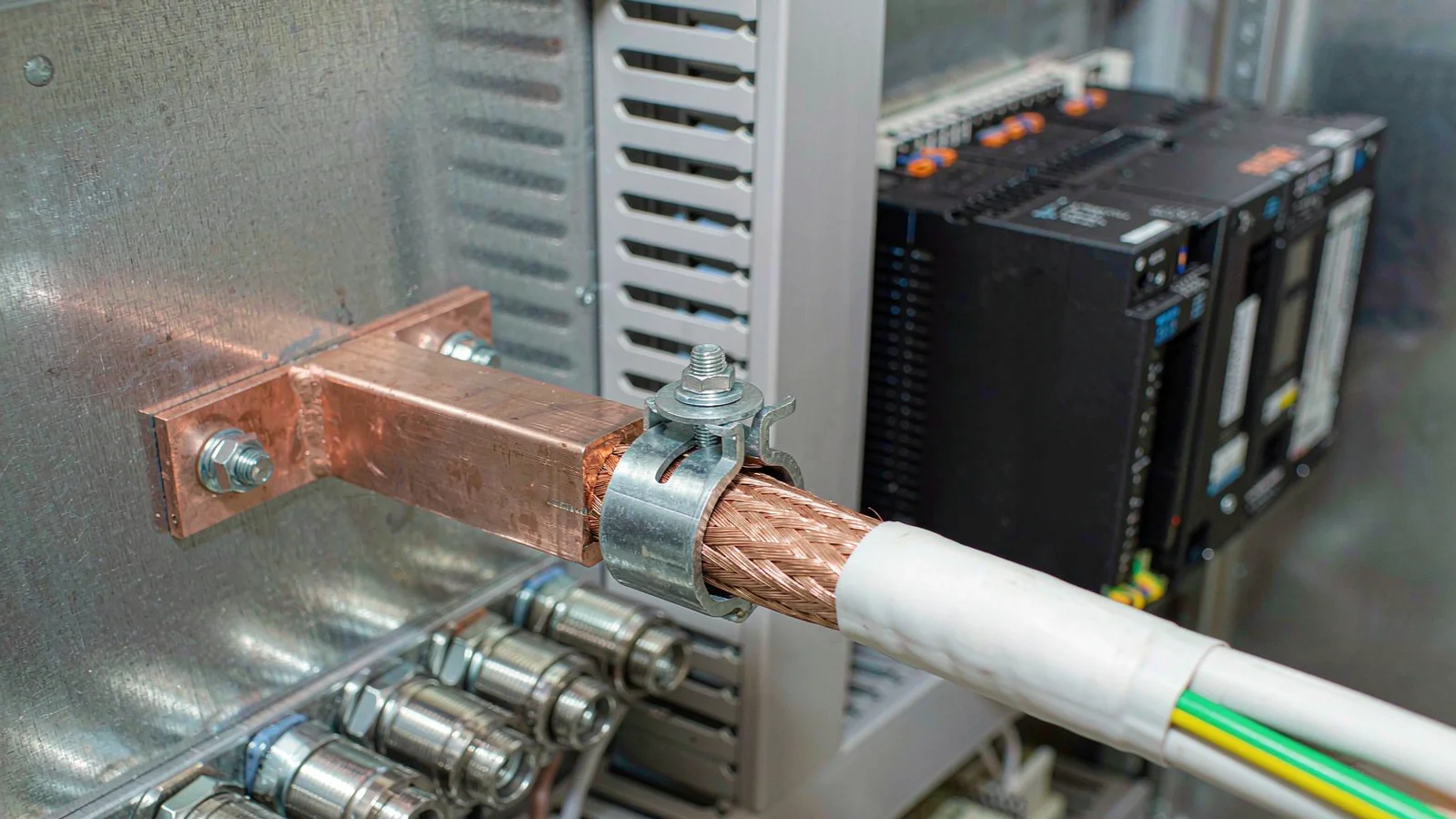 Copper earth bar with a shielded cable screen clamped to it beside a row of glands in a control cabinet