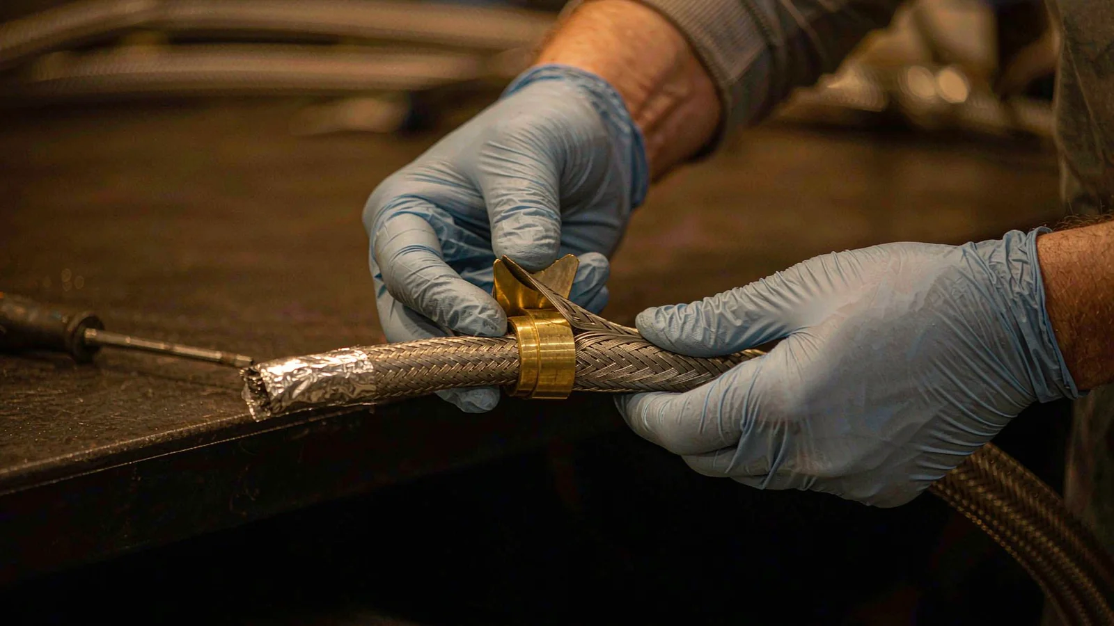 Gloved hands folding a braided cable screen back over the insert of a brass cable gland