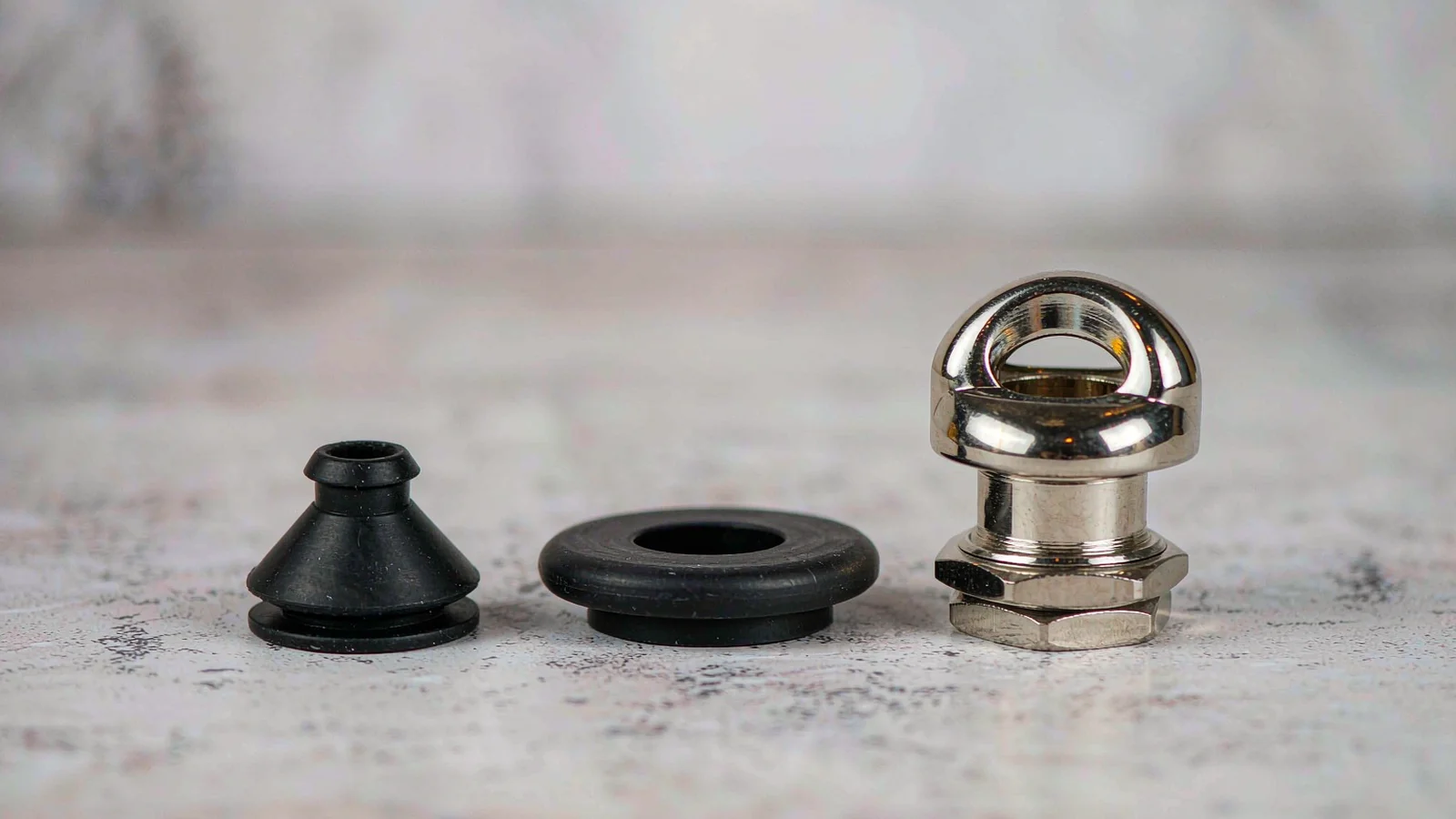 Black rubber cable seal insert, flat rubber face washer and nickel-plated brass cable gland body on a workbench