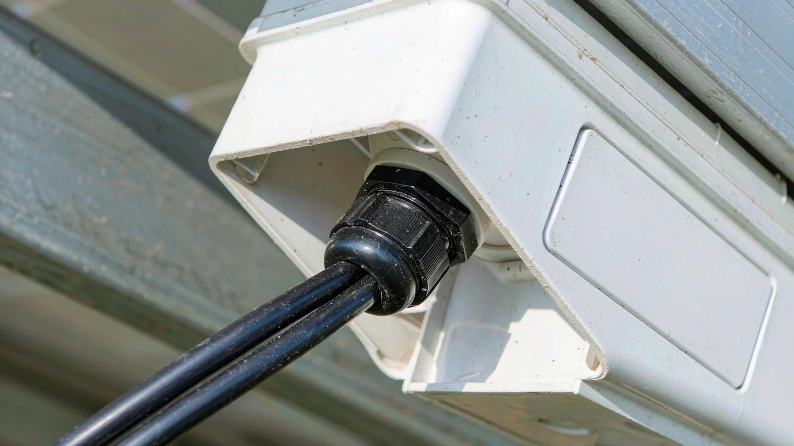 Solar string cable entering the underside of a module junction box through a black cable gland on a rooftop array